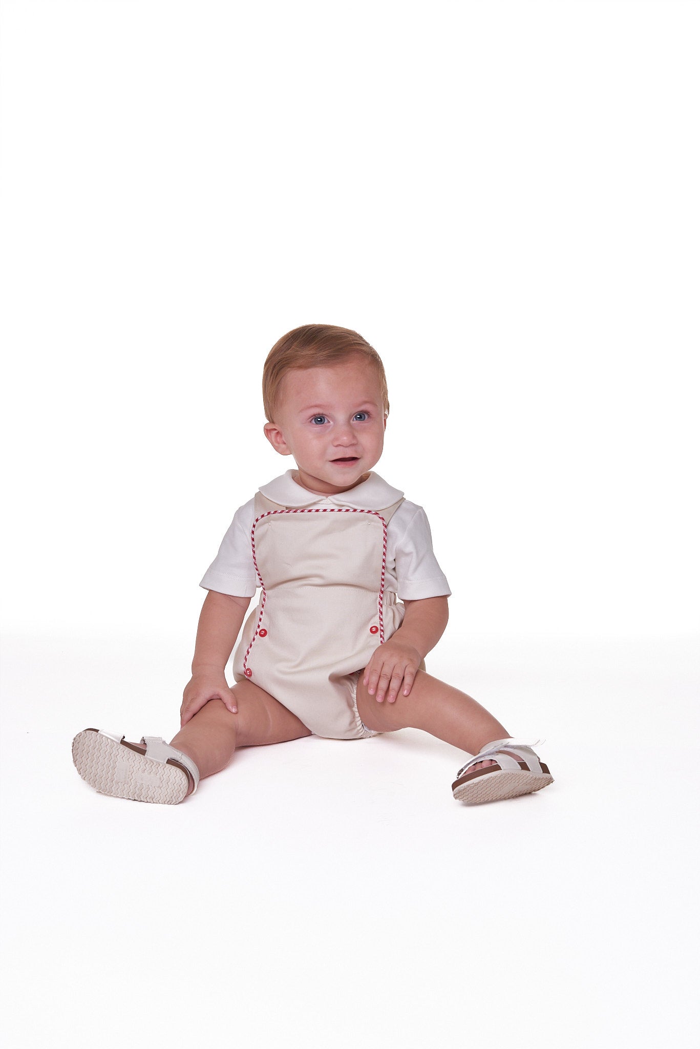 Jardineira Liam em sarja bege com vermelho e azul, edição especial. Clássica, confoável e ideal para bebês de 3 a 18 meses.
