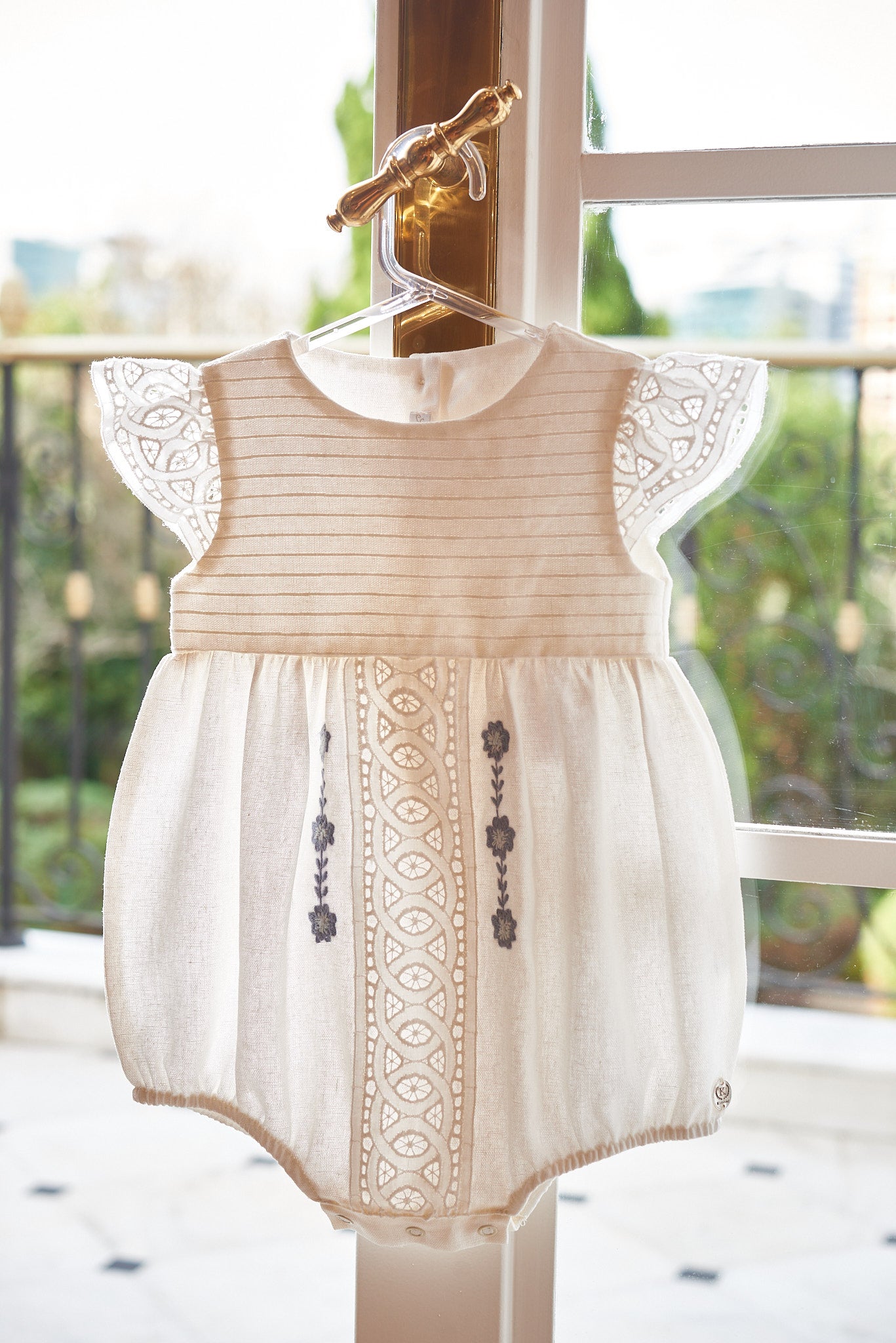 Bombacho Mirela em linho com bordado azul, babados delicados e botões nas costas e entrepernas. Elegância e conforto para bebês de 3 a 18 meses.

