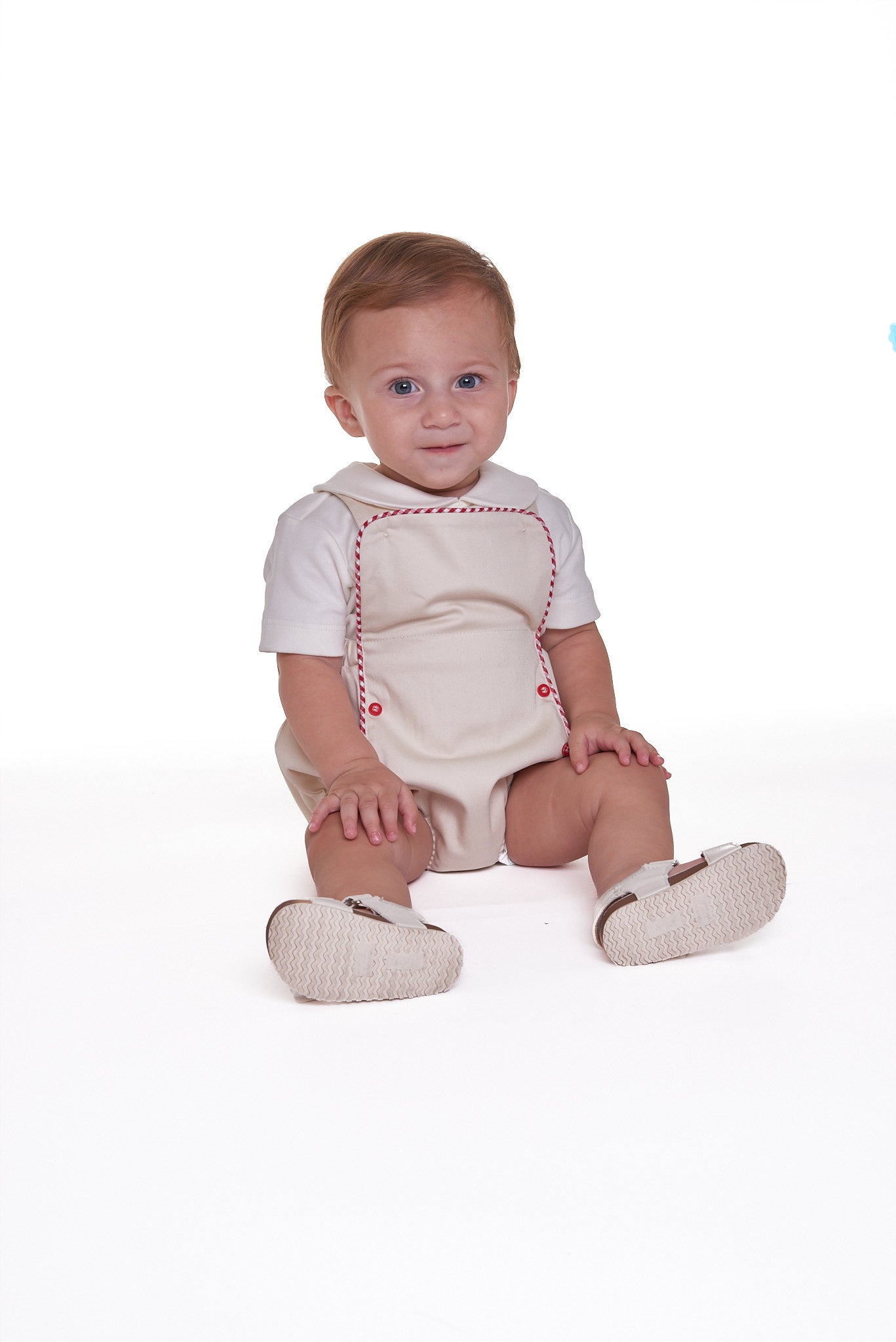 Jardineira Liam em sarja bege com vermelho e azul, edição especial. Clássica, confortável e ideal para bebês de 3 a 18 meses.

