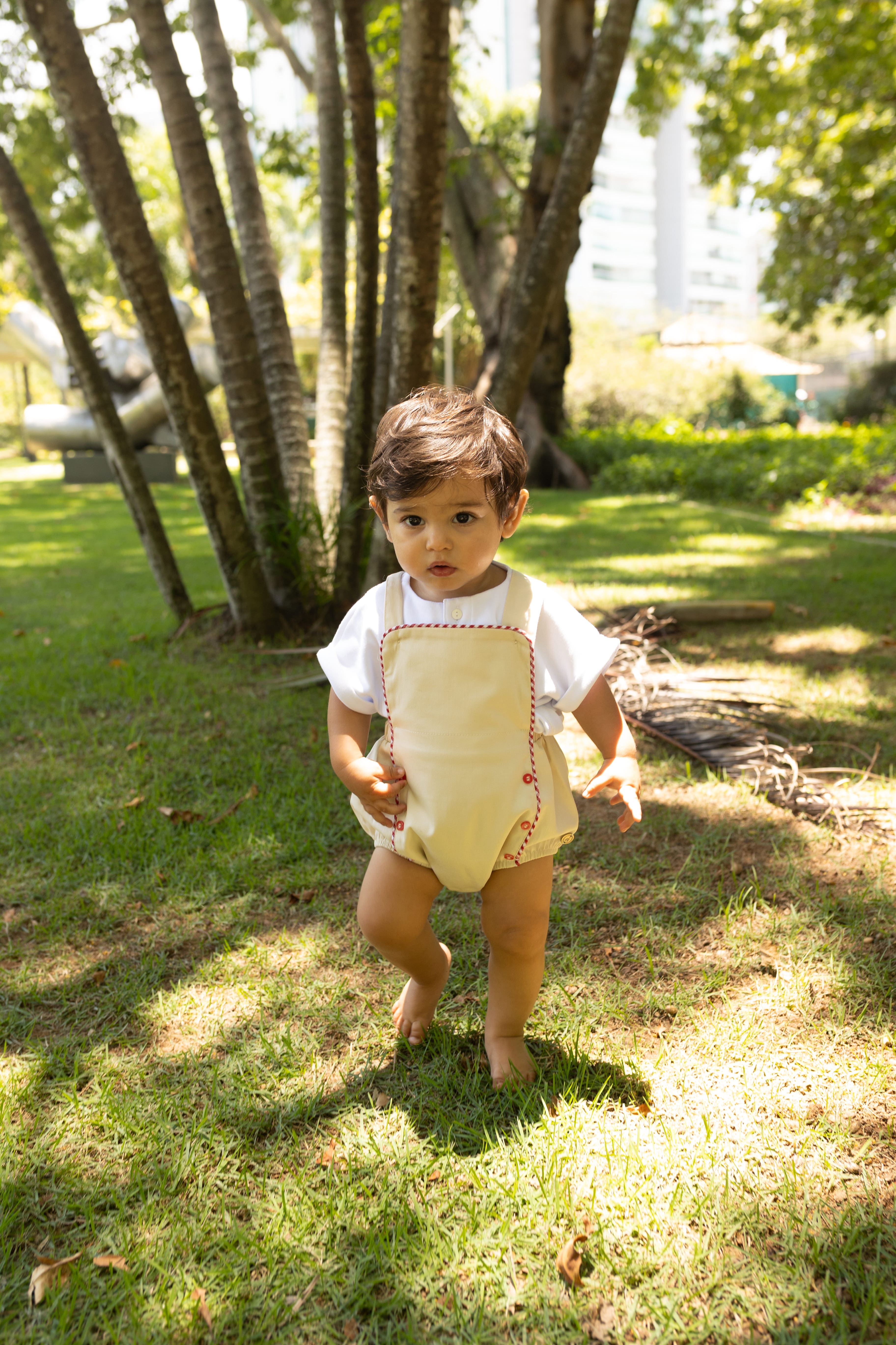 Jardineira Liam em sarja bege com vermelho e azul, edição especial. Clássica, confortável e ideal para bebês de 3 a 18 meses.