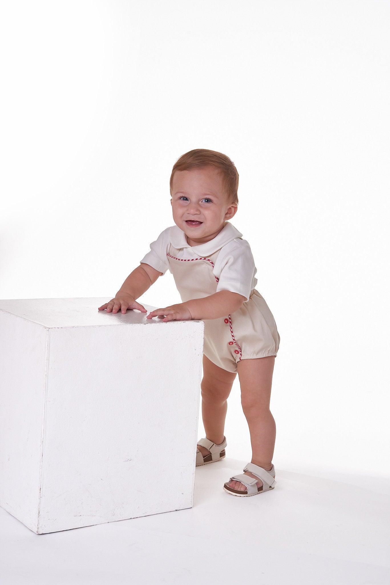 Jardineira Liam em sarja bege com vermelho e azul, edição especial. Clássica, confortável e ideal para bebês de 3 a 18 meses.