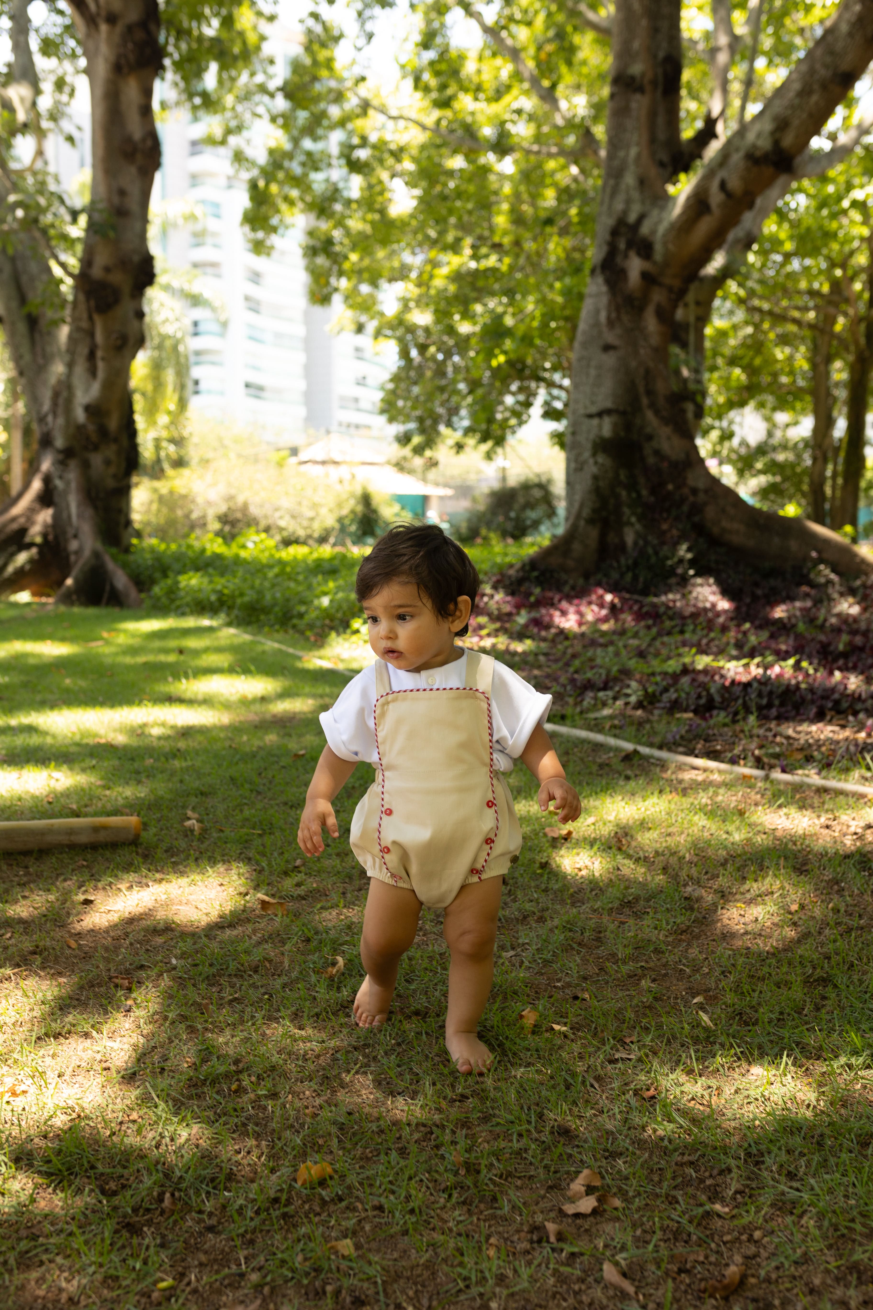 Jardineira Liam em sarja bege com vermelho e azul, edição especial. Clássica, confortável e ideal para bebês de 3 a 18 meses.

