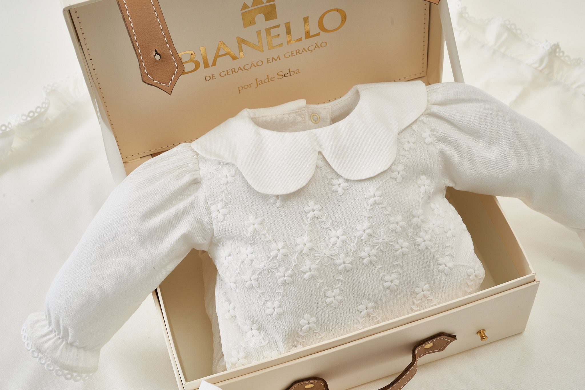 Macacão de bebê Rebeka em tricot com gola em renda bordada e laços nos pés.
