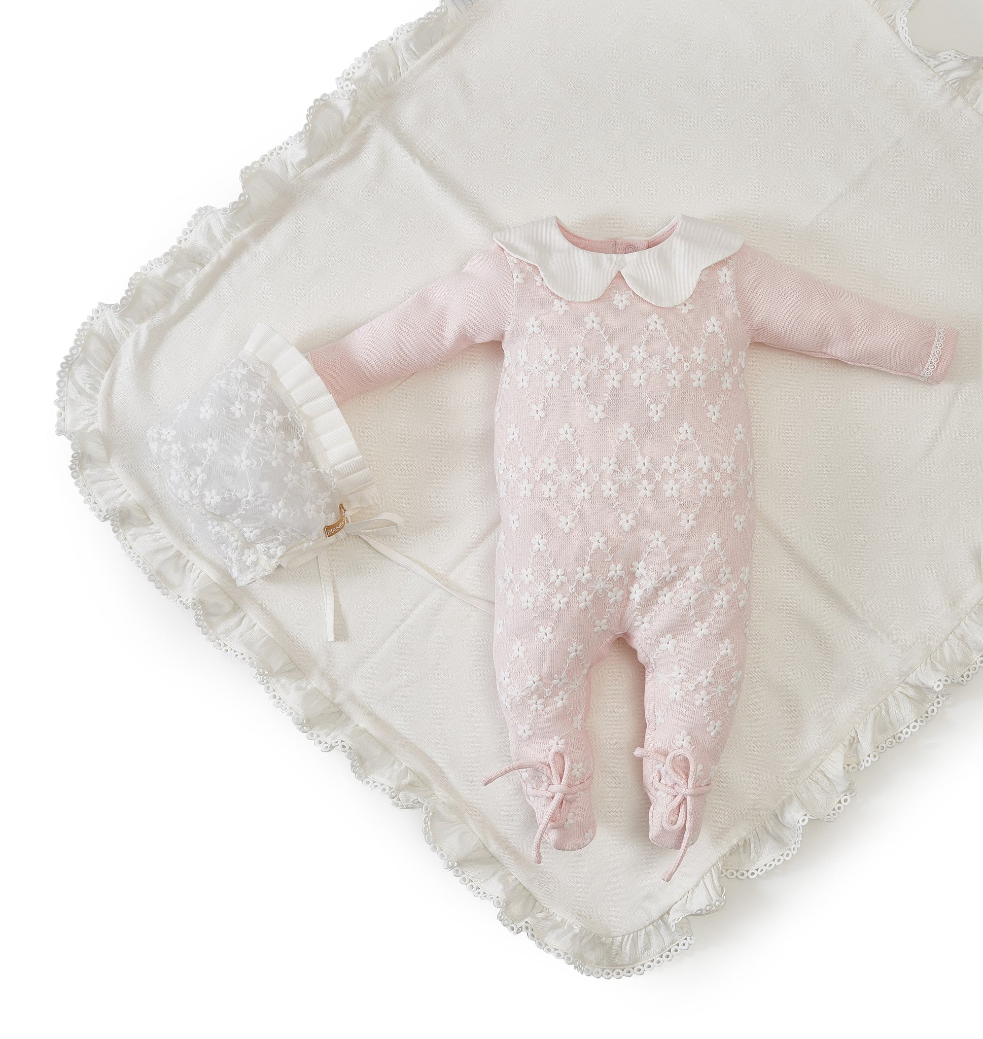 Macacão de bebê Rebeka em tricot com gola em renda bordada e laços nos pés.

