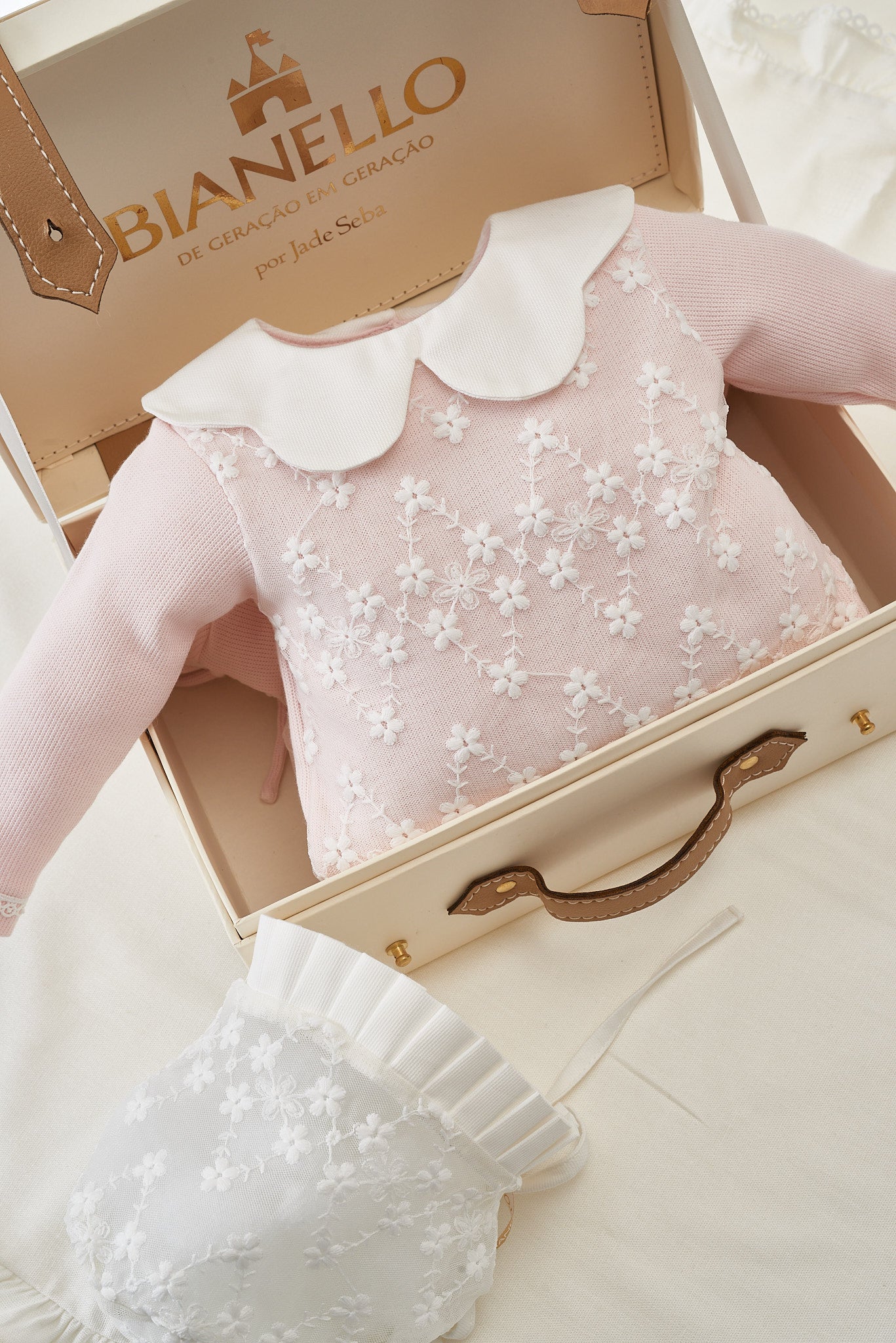 Macacão de bebê Rebeka em tricot com gola em renda bordada e laços nos pés.

